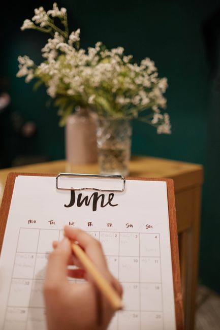 A hand marking a date on a paper calendar beside a clipboard.